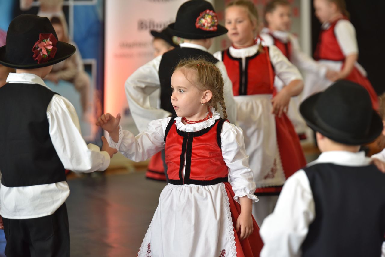 Young children dressed in traditional Hungarian attire perform a cultural dance indoors.