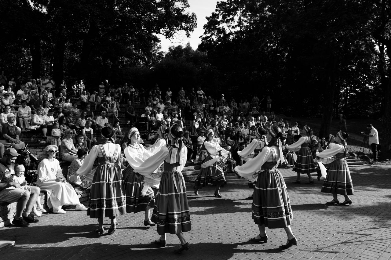 Black and white photo of dancers in traditional attire performing in front of an audience outdoors.