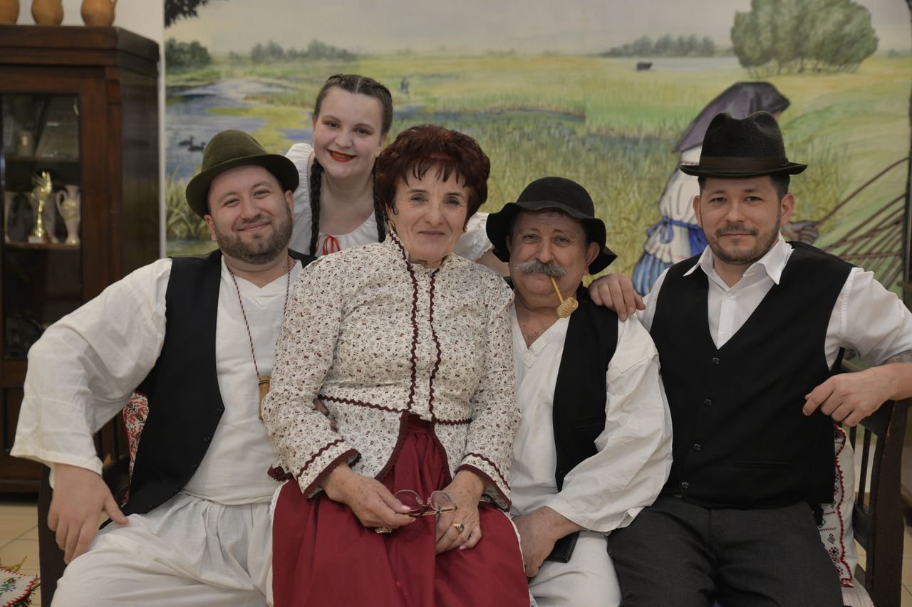 A Hungarian family dressed in traditional folk clothing poses indoors, exuding cultural heritage.